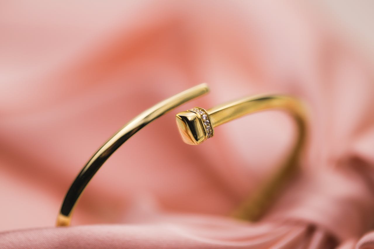 Close-up of a luxurious gold bracelet with diamonds, set against a soft pink fabric background.