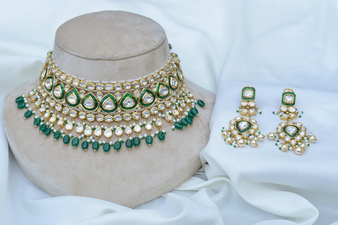 Luxurious gold and green jewelry set featuring intricate beadwork and pearls displayed on a fabric backdrop.