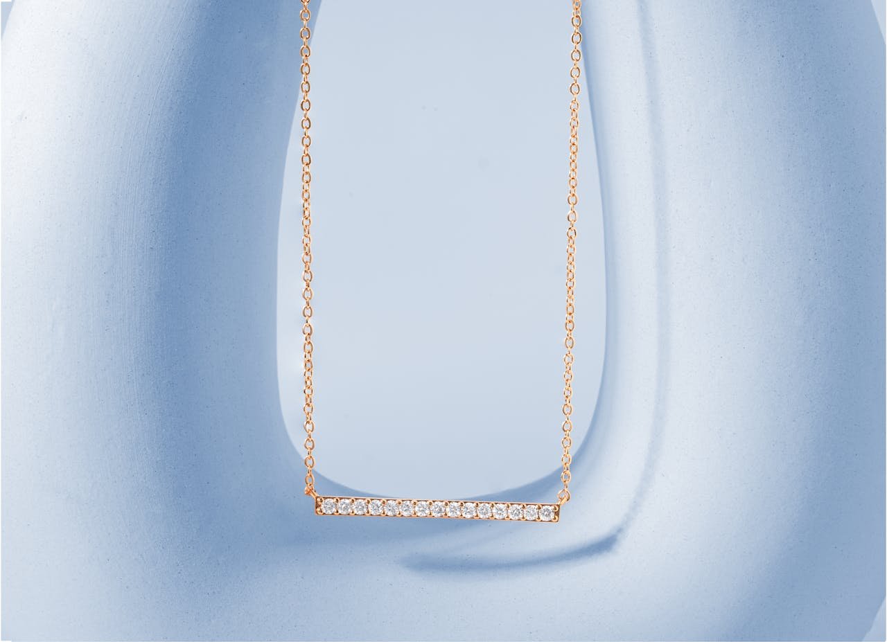 Close-up of a luxurious gold necklace with a diamond pendant on a light blue background, perfect for jewelry advertisements.