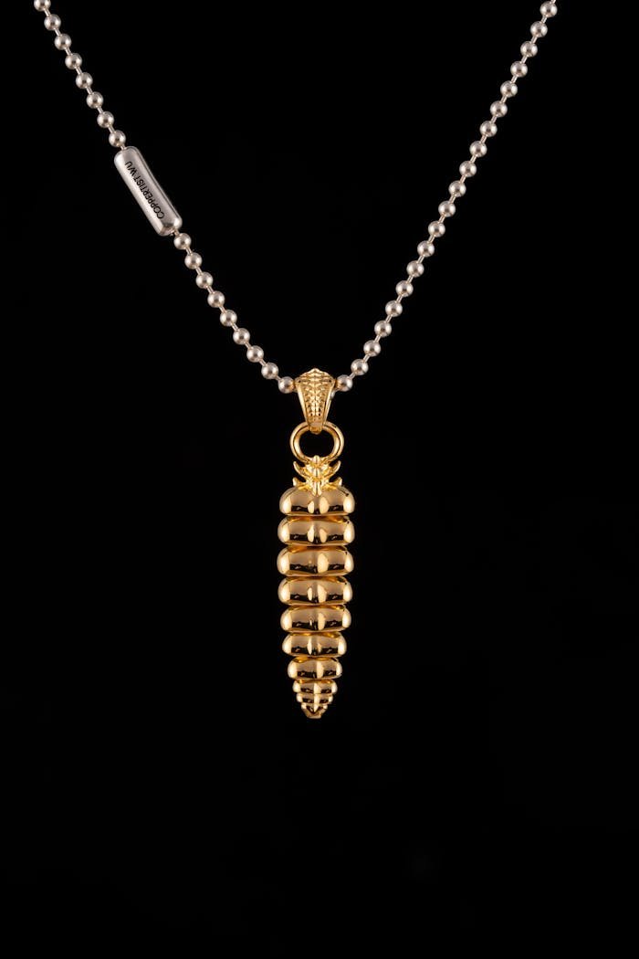 A striking gold pendant necklace set against a black backdrop, showcasing intricate design.