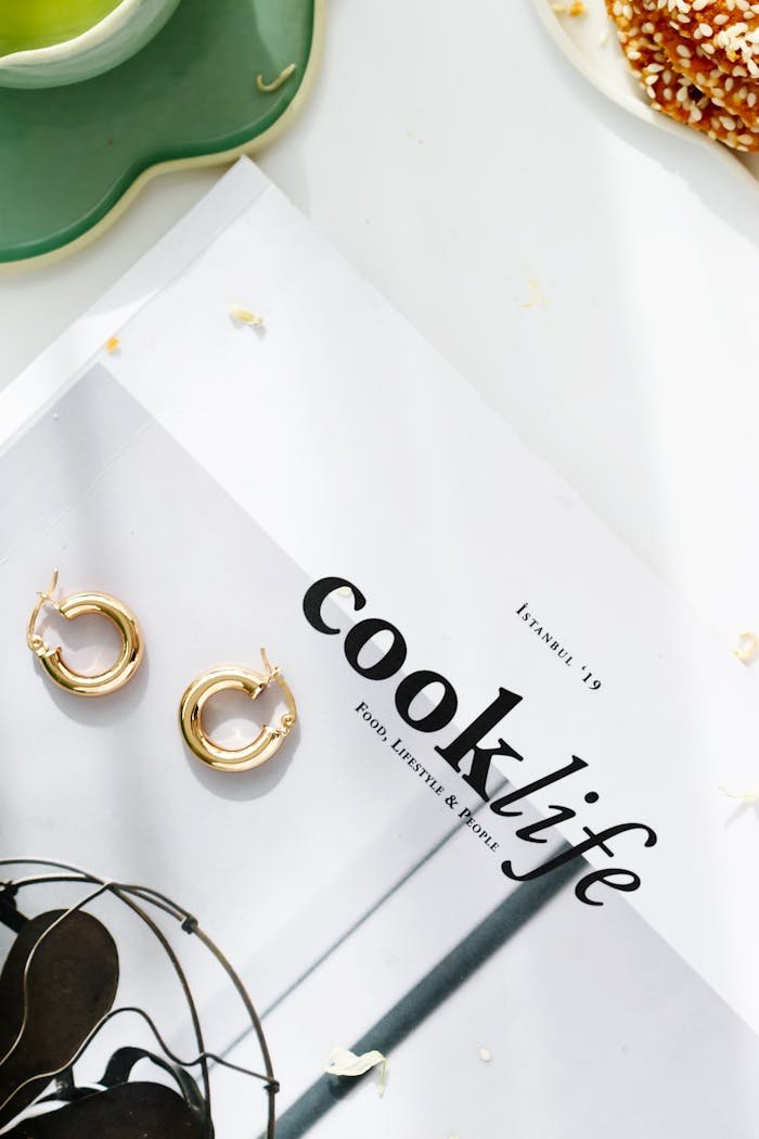 Gold hoop earrings placed on a trendy magazine with food and lifestyle themes.