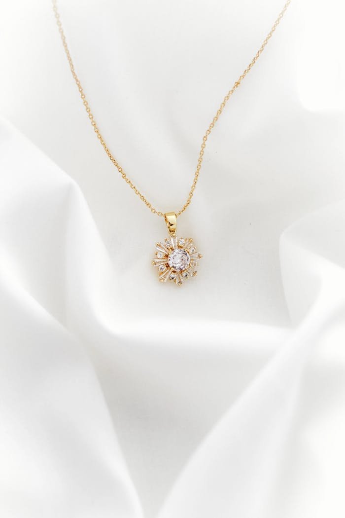 A stunning gold necklace with a delicate pendant on soft white fabric, exuding elegance.