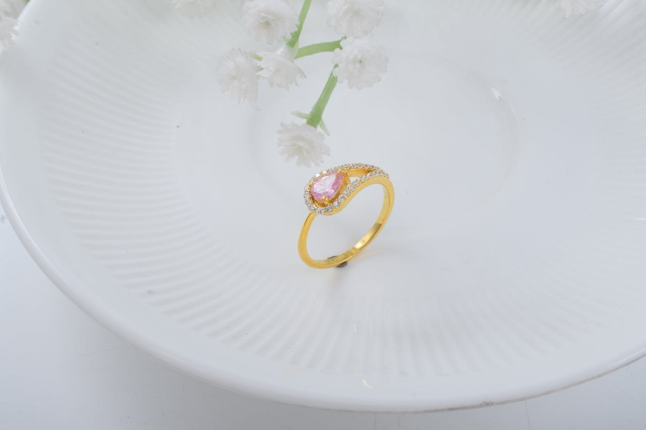 A close-up shot of a gold ring with a pink gemstone, elegantly placed on a white plate with floral accents.