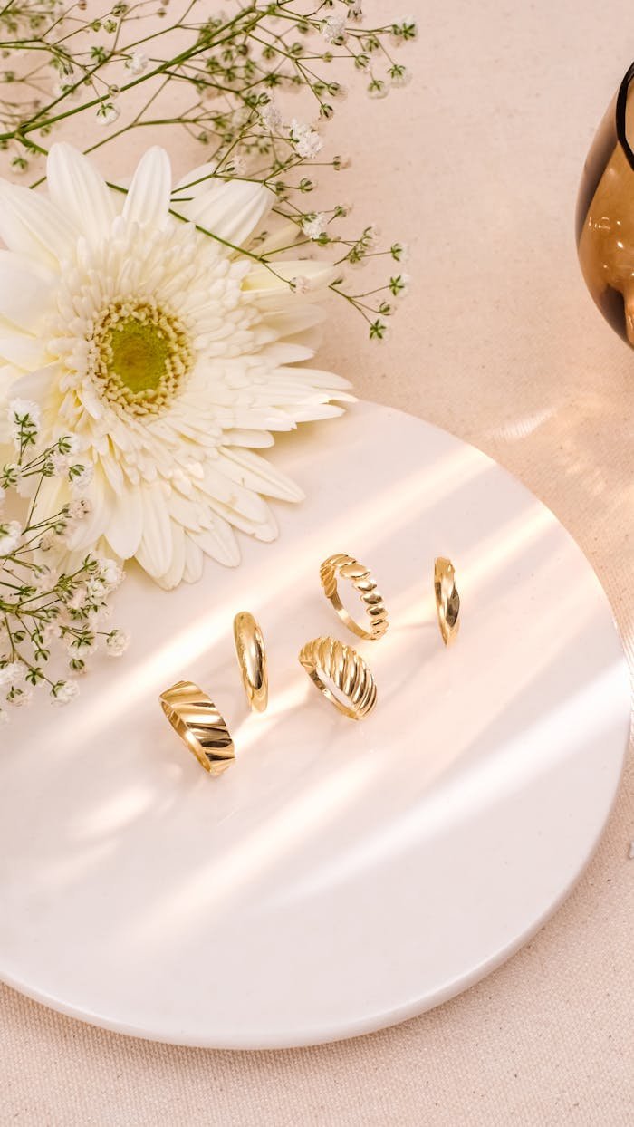 Chic gold rings on a white plate, accented by a white flower on a soft background.
