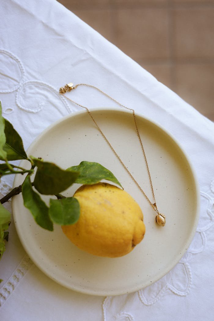 Close-up of a gold necklace beside a lemon on a ceramic plate.