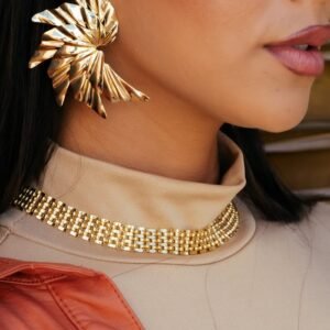 Close-up portrait highlighting chic gold earrings and necklace on a stylish woman.
