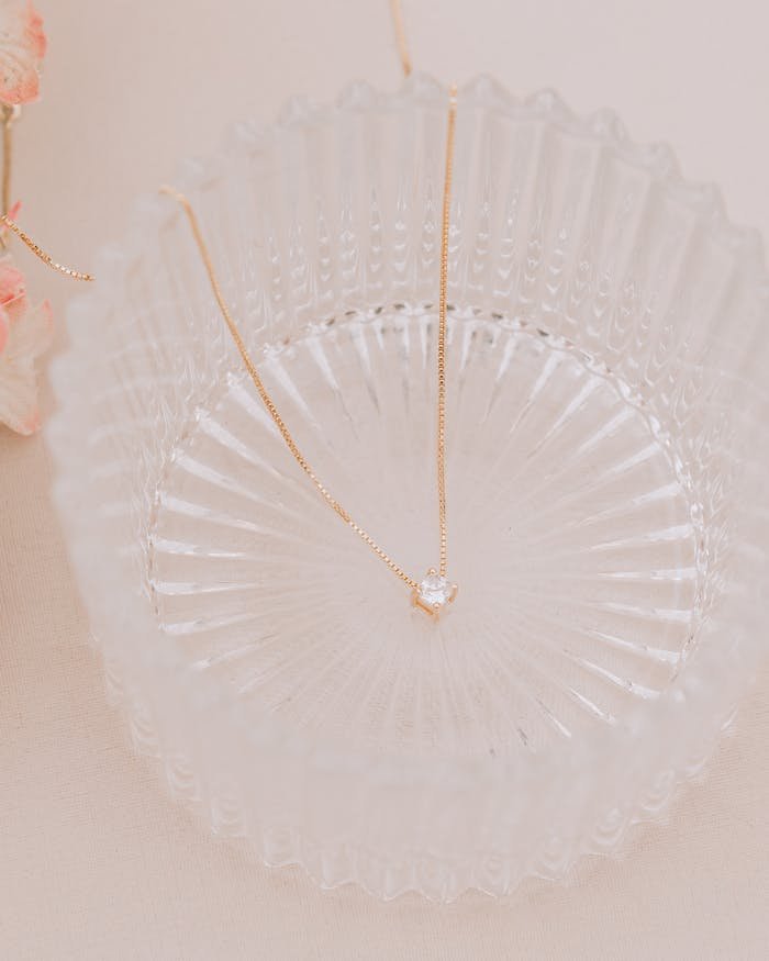 Delicate diamond necklace displayed on a textured glass plate with floral accents.