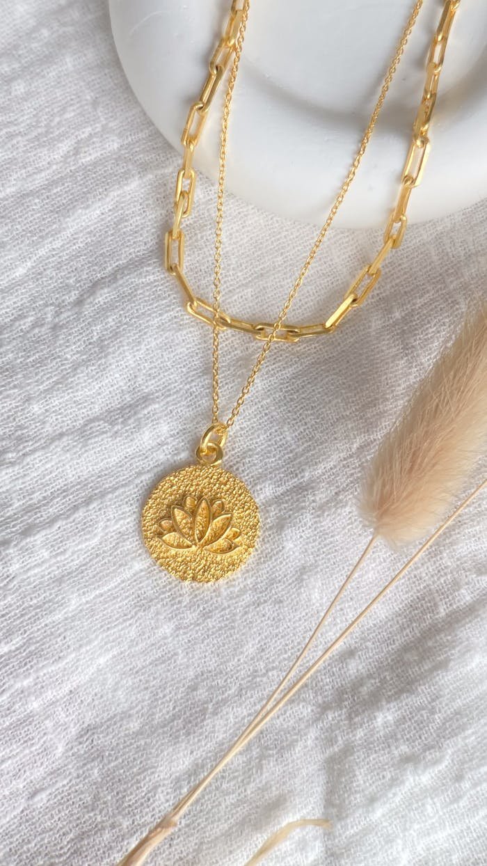 Stylish gold necklace with lotus pendant on white textured fabric, elegant and minimalistic design.