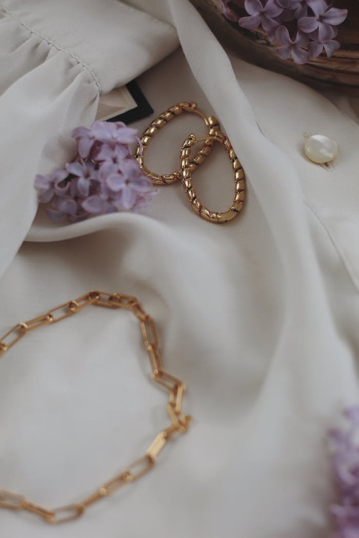 Stylish close-up of gold jewelry set against a light fabric with purple flowers, exuding elegance.