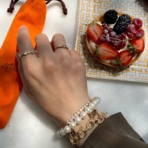 Close-up of hand with bracelets and a fruit tart on the table, in a luxury setting.