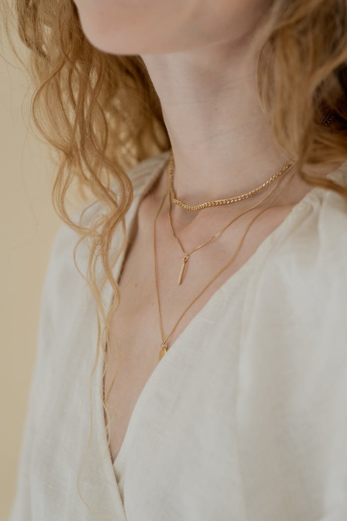 Close-up of elegant gold necklaces worn by a woman in soft natural lighting.